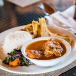 Home Delicious traditional Ugandan meal featuring rice, stew, greens, and chapati on a dining table.