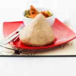 Home A traditional Nigerian dish elegantly presented on a vibrant red plate, accompanied by a colorful vegetable stew.